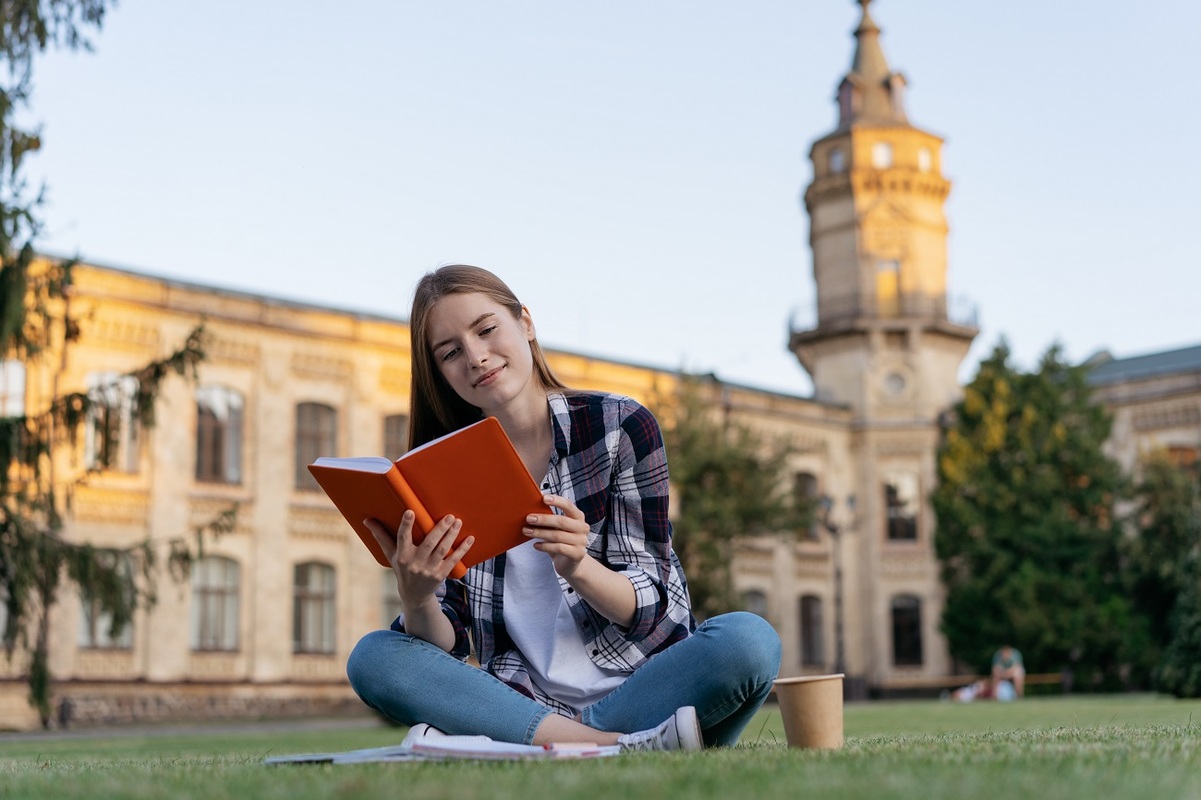 University student studying reading book learning language exam preparation sitting grass education concept